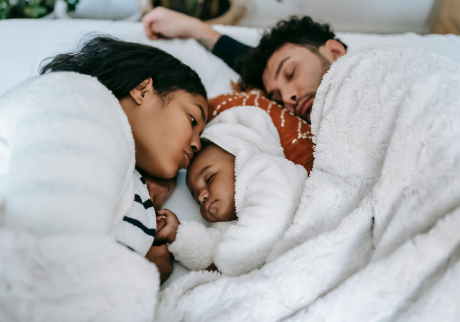 two parents laying in bed with a sleeping toddler